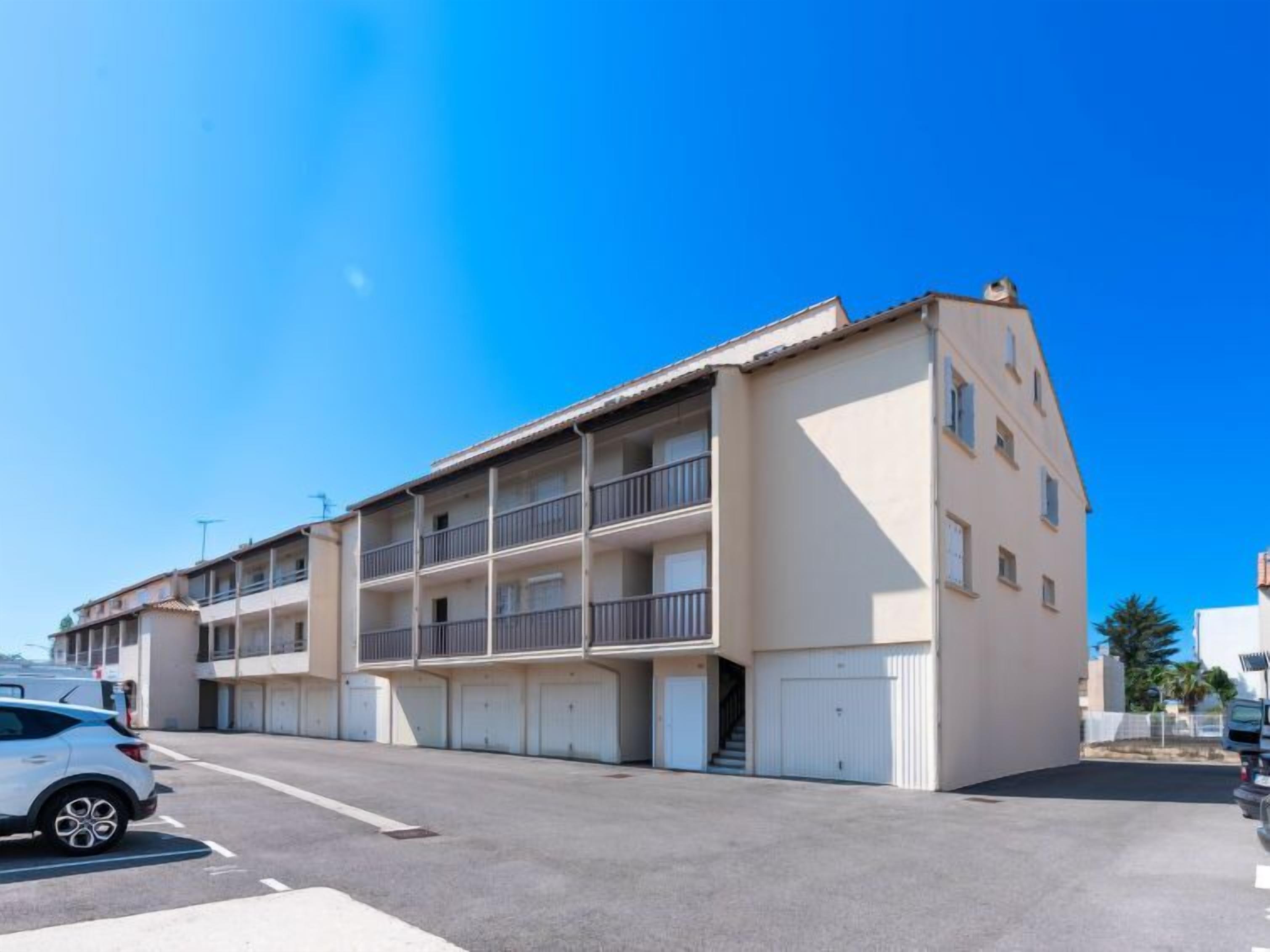 A multi-story building with balconies, a parking area, and a clear blue sky.