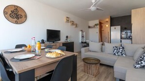 Un salon moderne avec une table à manger en bois, des chaises noires, un canapé blanc et un ventilateur de plafond.