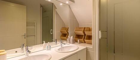 Un baño moderno con dos lavamanos, un espejo grande y estantes de madera empotrados.