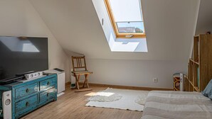 Un dormitorio con techo inclinado, tragaluz, televisor, cómoda, silla, cama y estantería.
