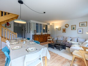 A dining area with a table set for four, a wooden staircase, and a living room with a sofa and a coffee table.