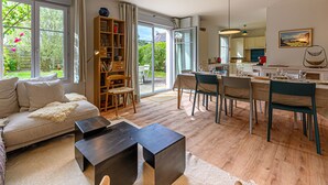 Un salón amplio con sofá, mesa de centro y estantería. Hay una zona de comedor con sillas y una mesa dispuesta para comer.