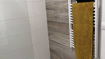 A bathroom with white tiles, a wooden wall, a towel rack with two towels, and a wooden bath mat.