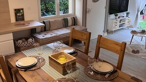 Ein Essbereich mit einem Holztisch, gedeckt für vier Personen, einer Couch mit Kissen, einem Fernseher und einem Fenster mit Vorhängen.