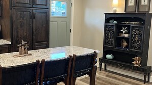 A kitchen with dark wooden cabinets, a marble countertop, and a dining area with dark woven chairs.