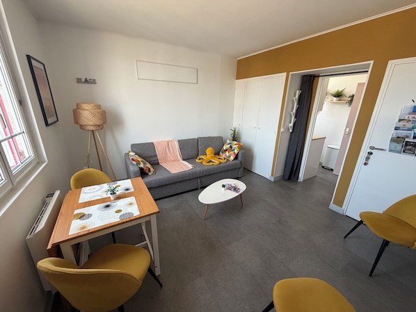A modern living room with a sofa, a coffee table, and two yellow chairs. There is a small table with a decorative item and a lamp.