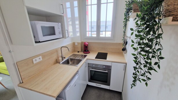 A compact kitchen with a microwave, sink, and oven. There is a window with a view of buildings outside.