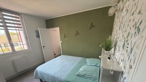 A bedroom with a bed, a window, a door, a wall with a bird mural, and a plant on a shelf.