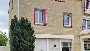 A two-story building with a brick facade, red window shutters, and a gravel driveway.