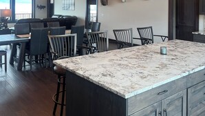 Una cocina amplia con una isla grande, lámparas colgantes modernas y un comedor con sillas de cuero oscuro.
