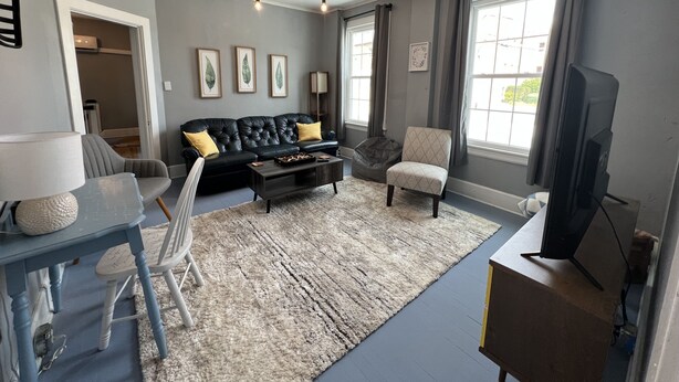 Ein Wohnzimmer mit einem schwarzen Ledersofa, einem gemusterten Sessel, einem Couchtisch und einem Fernseher.