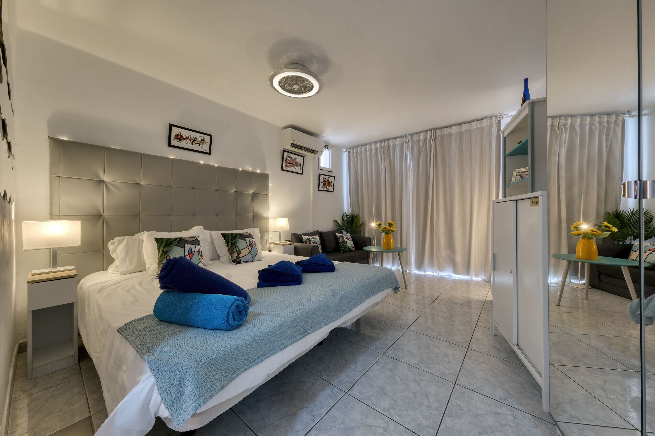 A modern hotel room with a large bed, a bedside table with a lamp, a wardrobe, and a small table with a vase of flowers.