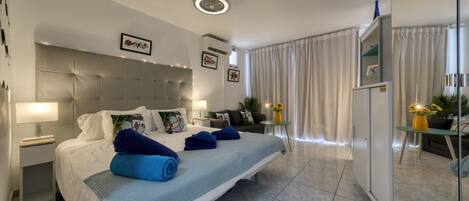 A modern hotel room with a large bed, a bedside table with a lamp, a wardrobe, and a small table with a vase of flowers.