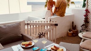 Ett par på en balkong med utsikt över havet, där ett bord är dukat med mat och dryck.