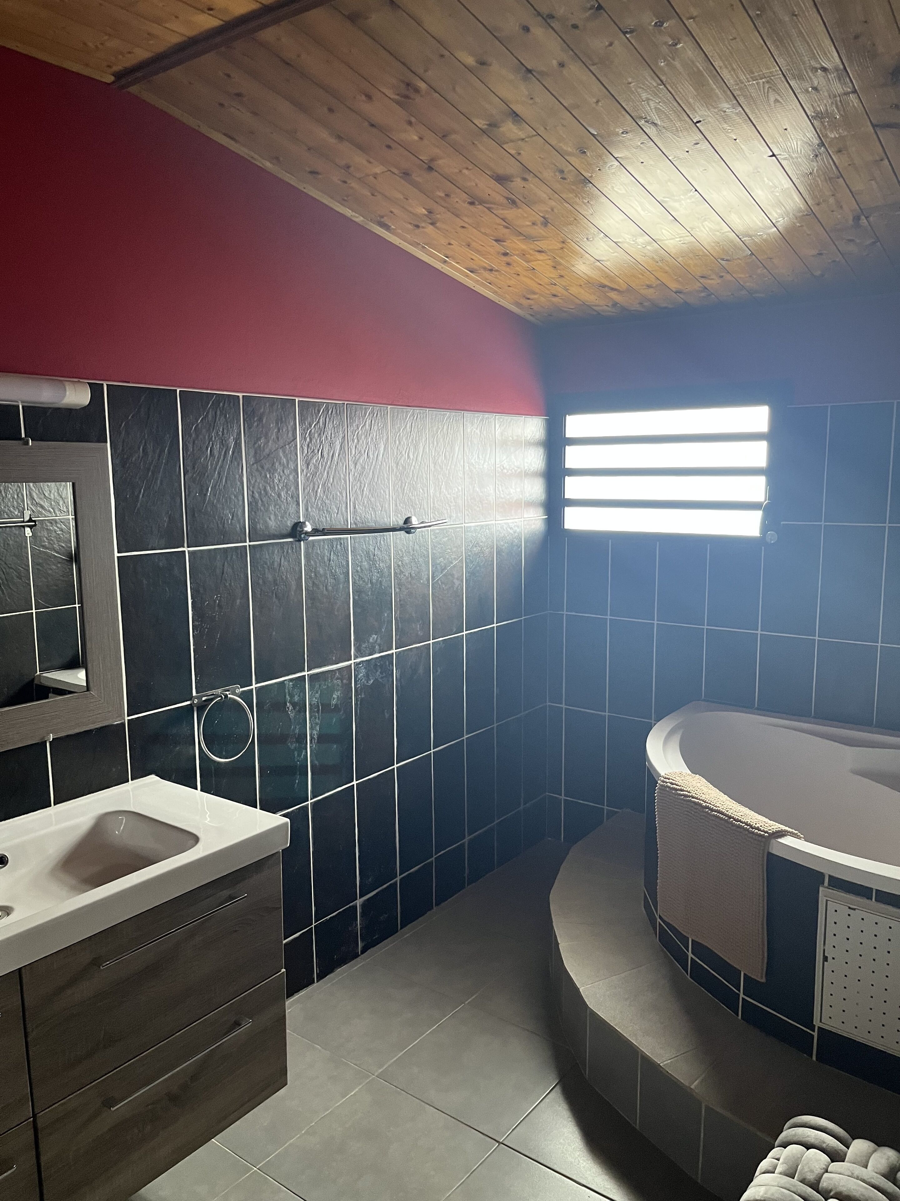 A bathroom with a wooden ceiling, a bathtub, a sink, and a towel rack.