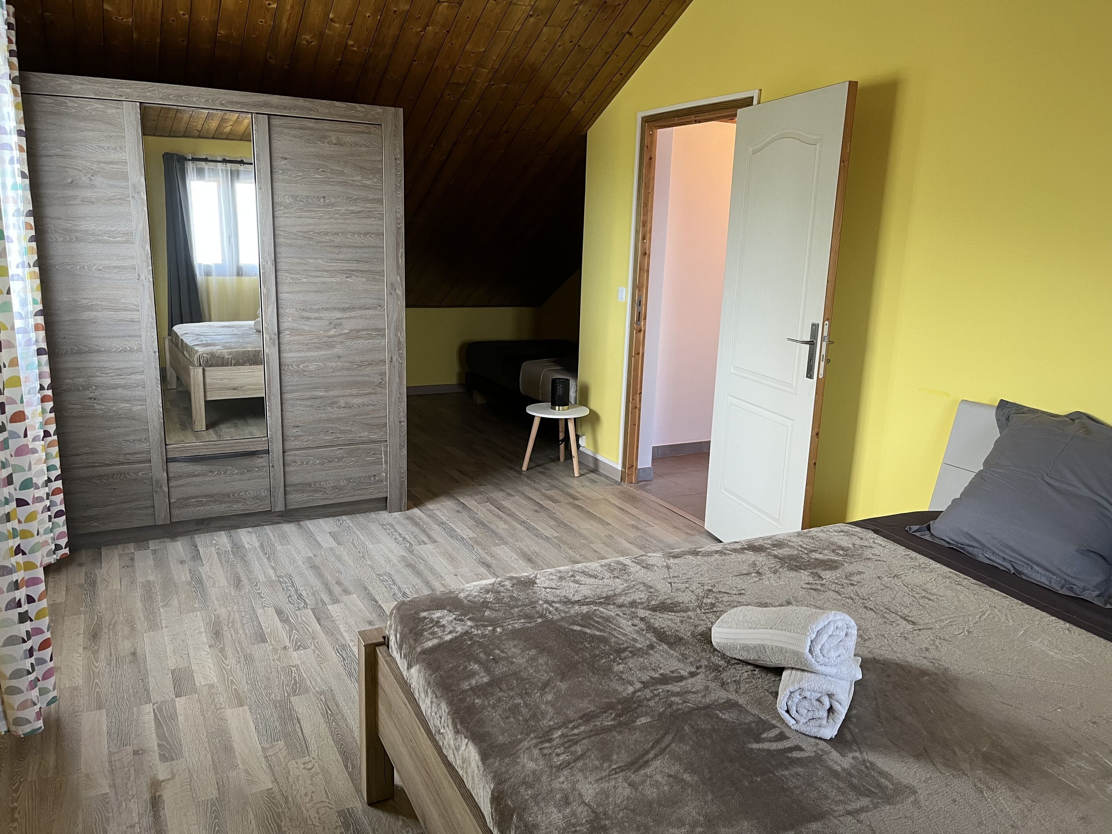 Quarto com cama de madeira, mesa de cabeceira pequena, cadeira e guarda-roupa.