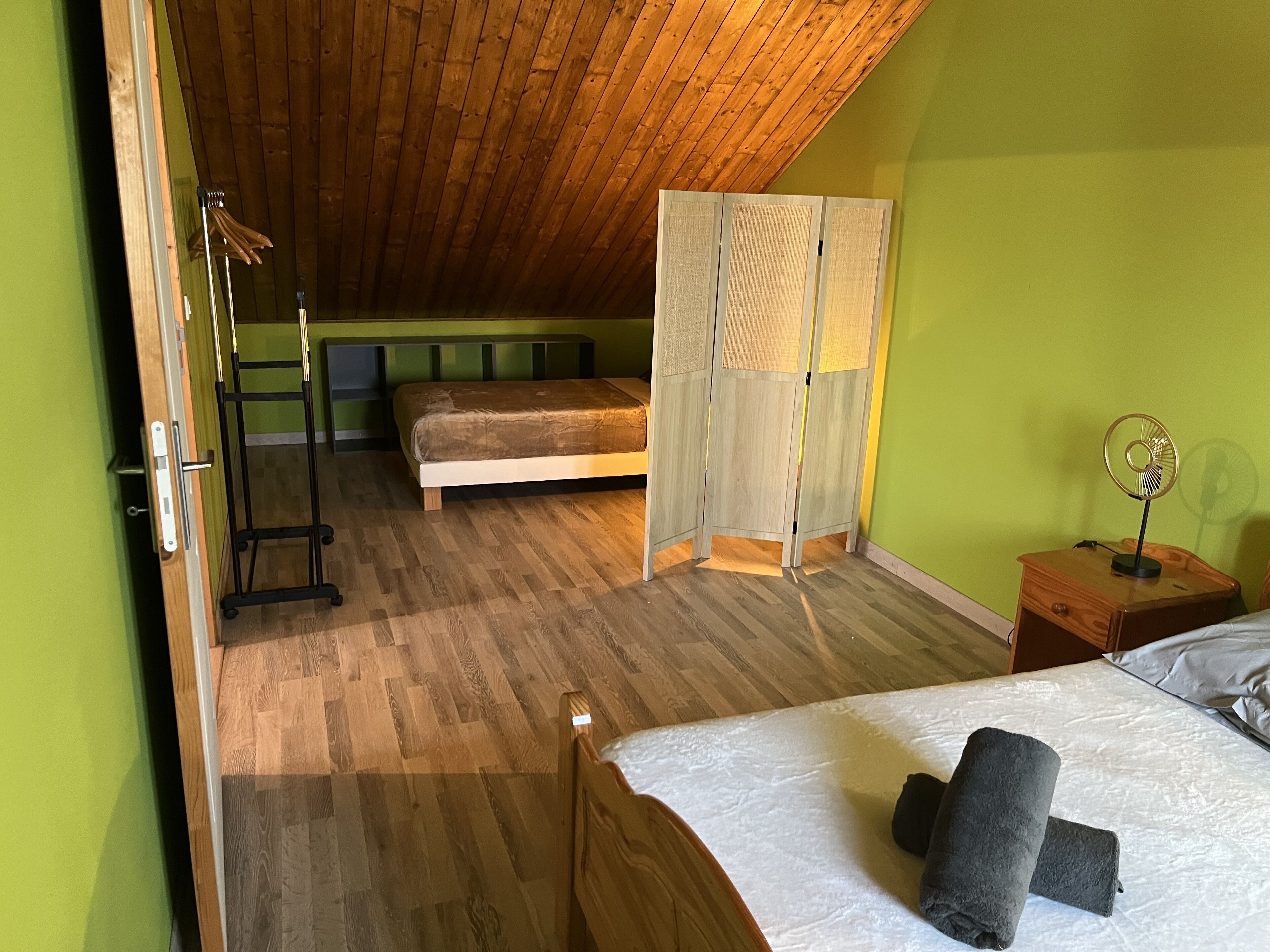 Una stanza con letto a soppalco, soffitto in legno, parete verde e un piccolo comodino con una ventola.
