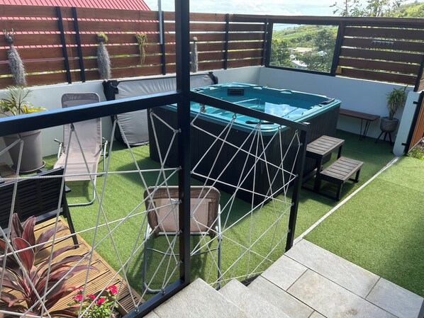 A rooftop patio with a hot tub, artificial grass, seating, and a view of the landscape.
