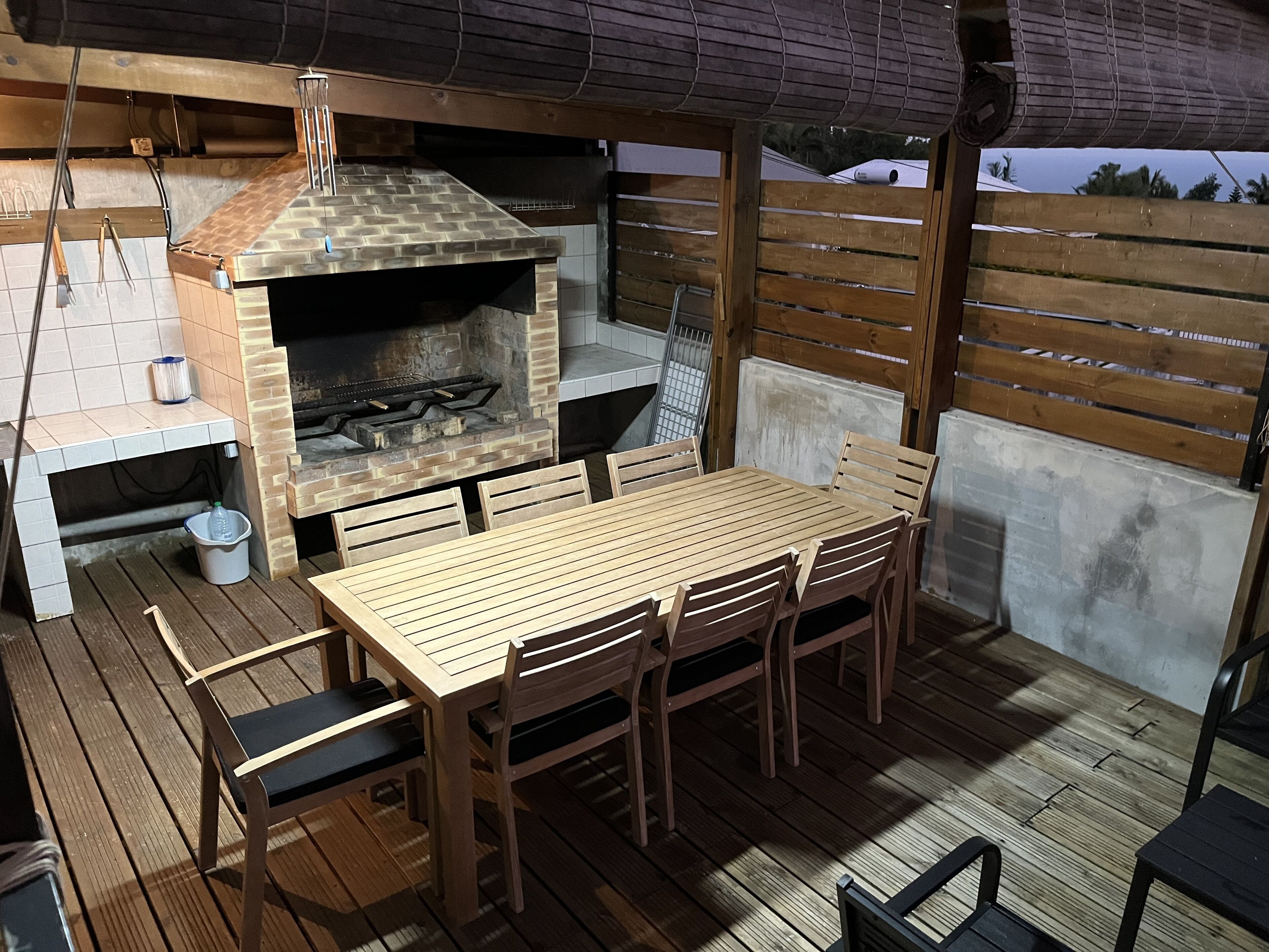 Un patio al aire libre con una mesa y sillas de madera, un horno de ladrillo y una parrilla.
