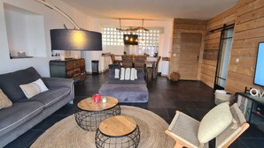 A modern living room with a grey sofa, two round coffee tables, a television, and a wooden accent wall. - 100m de la Plage,maison Face à la Mer! Idéale Pour de Belles Vacances en Famille (Brando)
