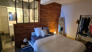 A bedroom with a wooden headboard, a bed with white bedding, a bedside table, a lamp, and a mirror. There is a clothing rack with various garments. - 100m de la Plage,maison Face à la Mer! Idéale Pour de Belles Vacances en Famille (Brando)