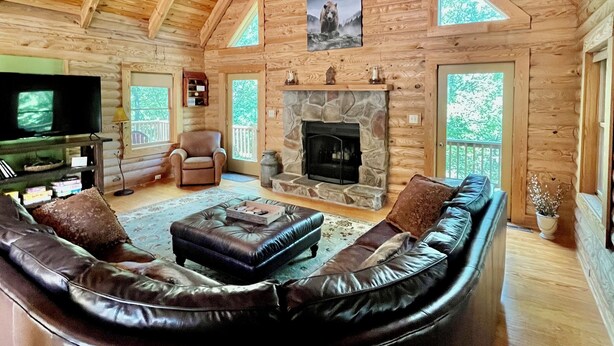 A log cabin interior with a stone fireplace, leather seating, a television, and a ceiling fan. - 5BR MOUNTAIN LODGE: 2MIN TO SLOPES, ARCADES FOOSBALL, GOLF WATERPARK, SLEEPS S14 (McGaheysville)