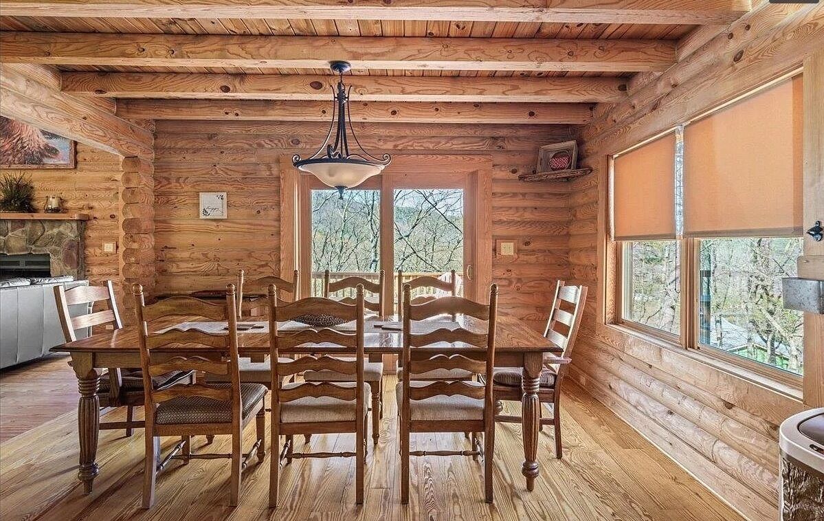 Un intérieur en bois avec une table et des chaises, un luminaire suspendu et des fenêtres donnant sur la forêt.