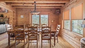 A wooden interior with a dining table and chairs, a hanging light fixture, and windows with a view of trees. - 5BR MOUNTAIN LODGE: 2MIN TO SLOPES, ARCADES FOOSBALL, GOLF WATERPARK, SLEEPS S14 (McGaheysville)