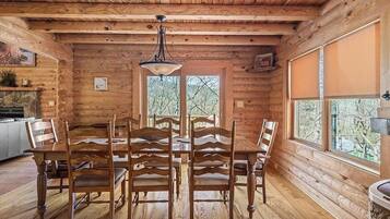 Un intérieur en bois avec une table et des chaises, un luminaire suspendu et des fenêtres donnant sur la forêt.