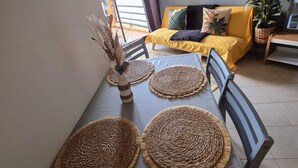 Un coin repas avec une table dressée pour quatre personnes, agrémenté de sets de table en fibres tressées et d’un vase contenant des branches séchées.
