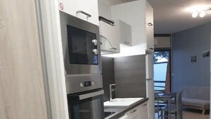 Une cuisine moderne dotée d’appareils électroménagers intégrés, un coin repas avec une table et des chaises, et une vue sur l’extérieur.