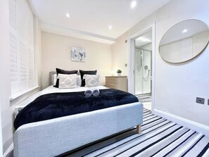 Ein modernes Schlafzimmer mit Bett, Nachttischen, einem Spiegel und einem begehbaren Kleiderschrank.