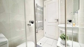 Een moderne badkamer met een douchecabine van glas, een wit toilet, een glazen deur en een witte wastafel met spiegel.