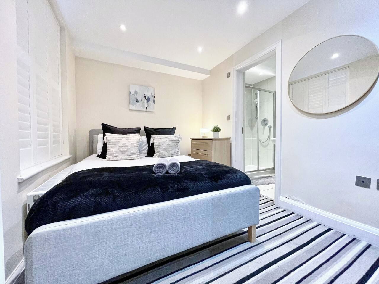 A modern bedroom with a bed, bedside tables, a mirror, and a walk-in closet.