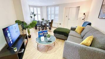A living room with a TV, a coffee table, a sofa, and a dining area with chairs and a table.