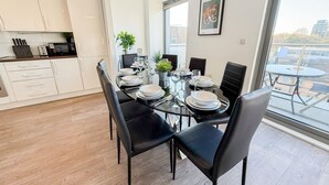 Uma área de jantar moderna com mesa de vidro, cadeiras pretas e pratos brancos.