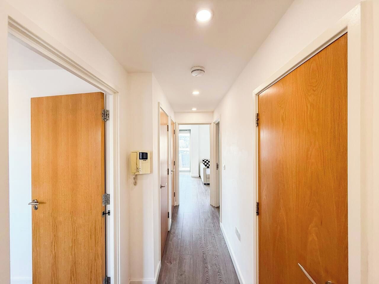 A hallway with wooden doors, a light switch, and a view into another room.