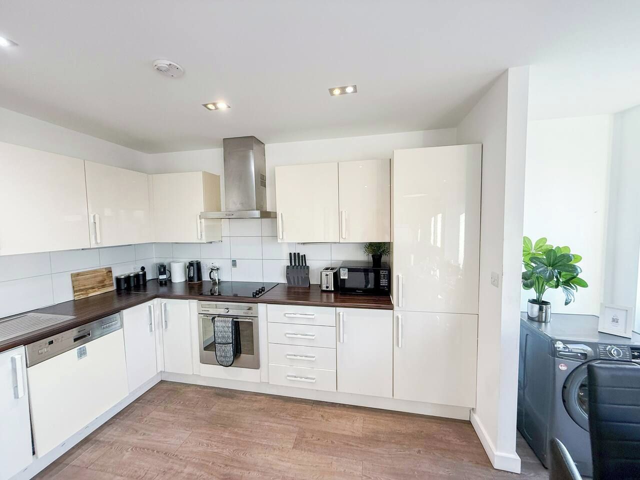 A modern kitchen with white cabinetry, a stainless steel range hood, and a built-in dishwasher.