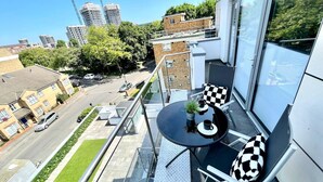 Un balcón con mesa y sillas, vista a la calle y un edificio al fondo.
