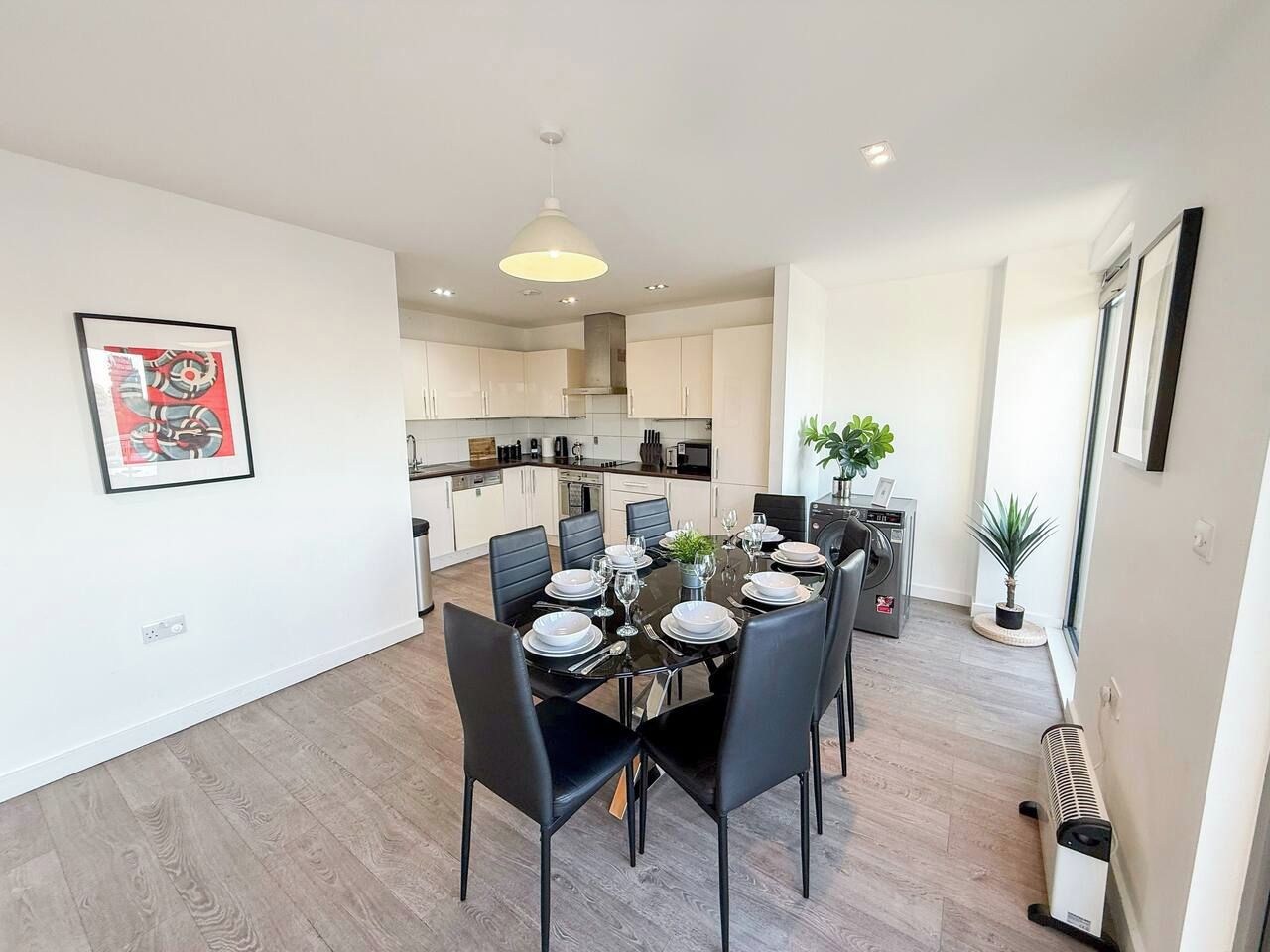 A modern kitchen with white cabinets, a dining table set for six, and a pendant light above.