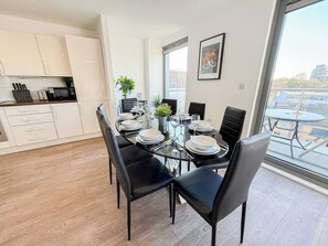 A modern dining area with a glass table set for four, black chairs, and a view of the city through large windows.