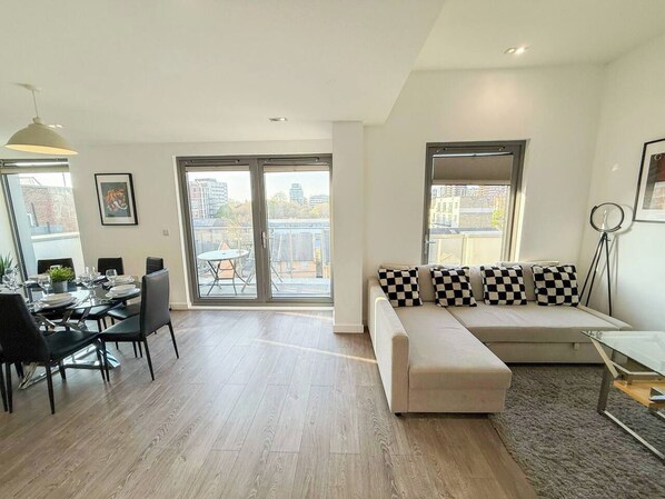 A modern living room with a dining area, large windows, and a sofa with checkered cushions.
