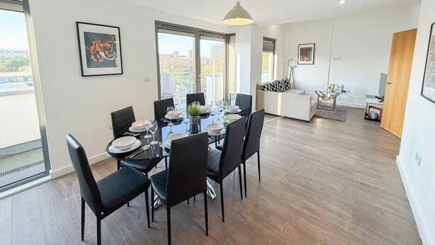 Un comedor moderno con una mesa redonda dispuesta para seis personas, rodeada de sillas negras. Hay un ventanal que ofrece vistas del paisaje urbano.