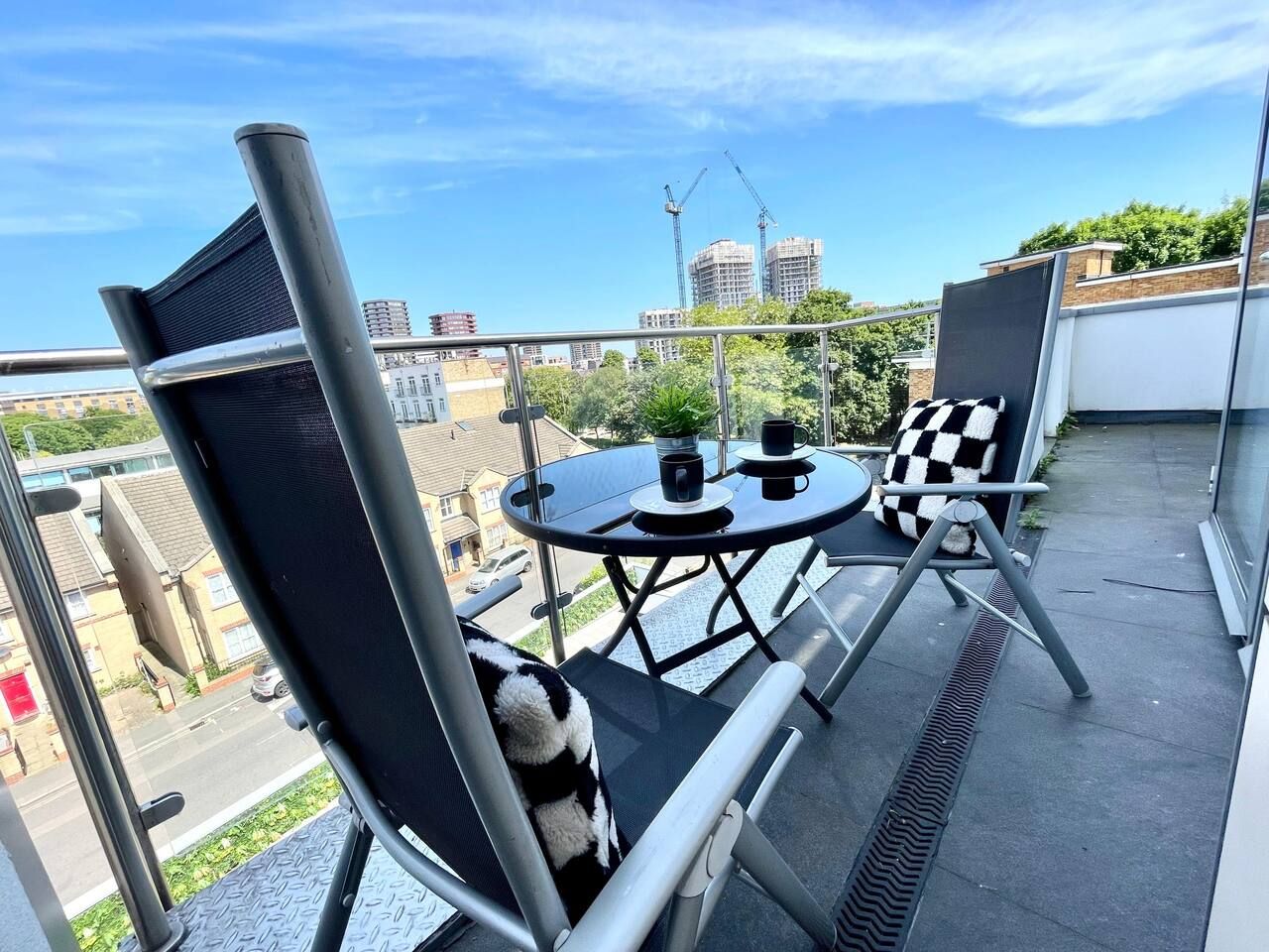 Een balkon met een tafel en stoelen, een uitzicht op de stad en een heldere lucht.