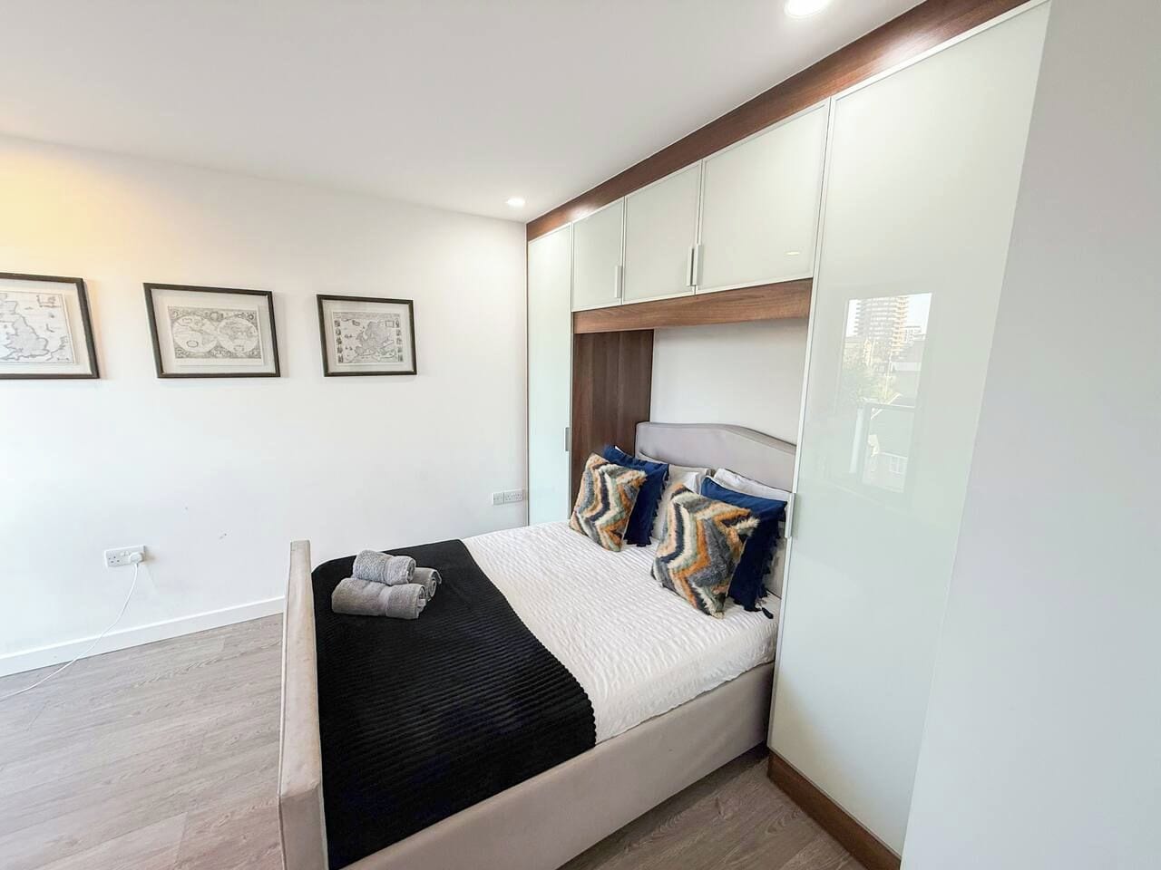A modern bedroom with a bed, headboard, wall-mounted cabinets, and framed artwork.