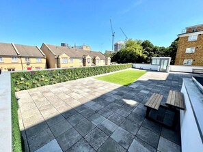 A rooftop terrace with a paved floor, a small grassy area, and a wooden bench. - 3bdr Hoxton Flat Near Old st, shoreditch + balcony (London)