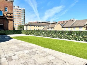 A residential area with a paved patio, a well-maintained lawn, and a row of terraced houses.