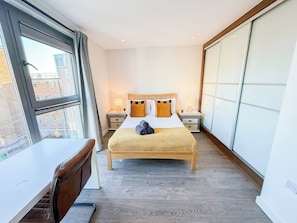 A hotel room with a bed, bedside tables, a desk, and a large window. - 3bdr Hoxton Flat Near Old st, shoreditch + balcony (London)