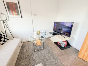 A living room with a sofa, a glass coffee table, a TV on a stand, and a framed picture on the wall.