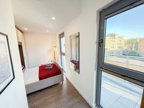 A bedroom with a bed, a window, and a view of buildings outside.